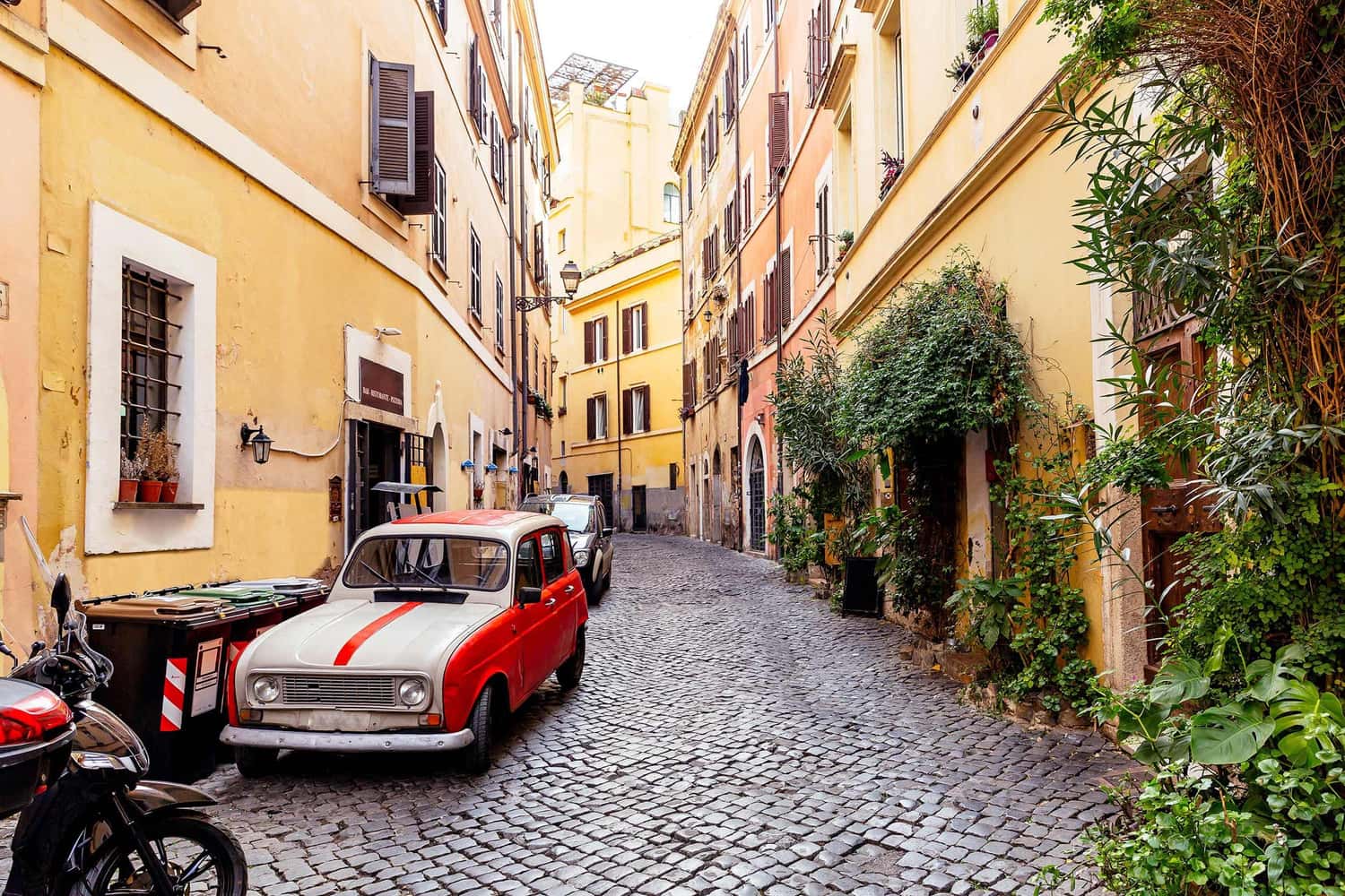 Vintage red car parked on narrow cobblestone street lined with colourful buildings
