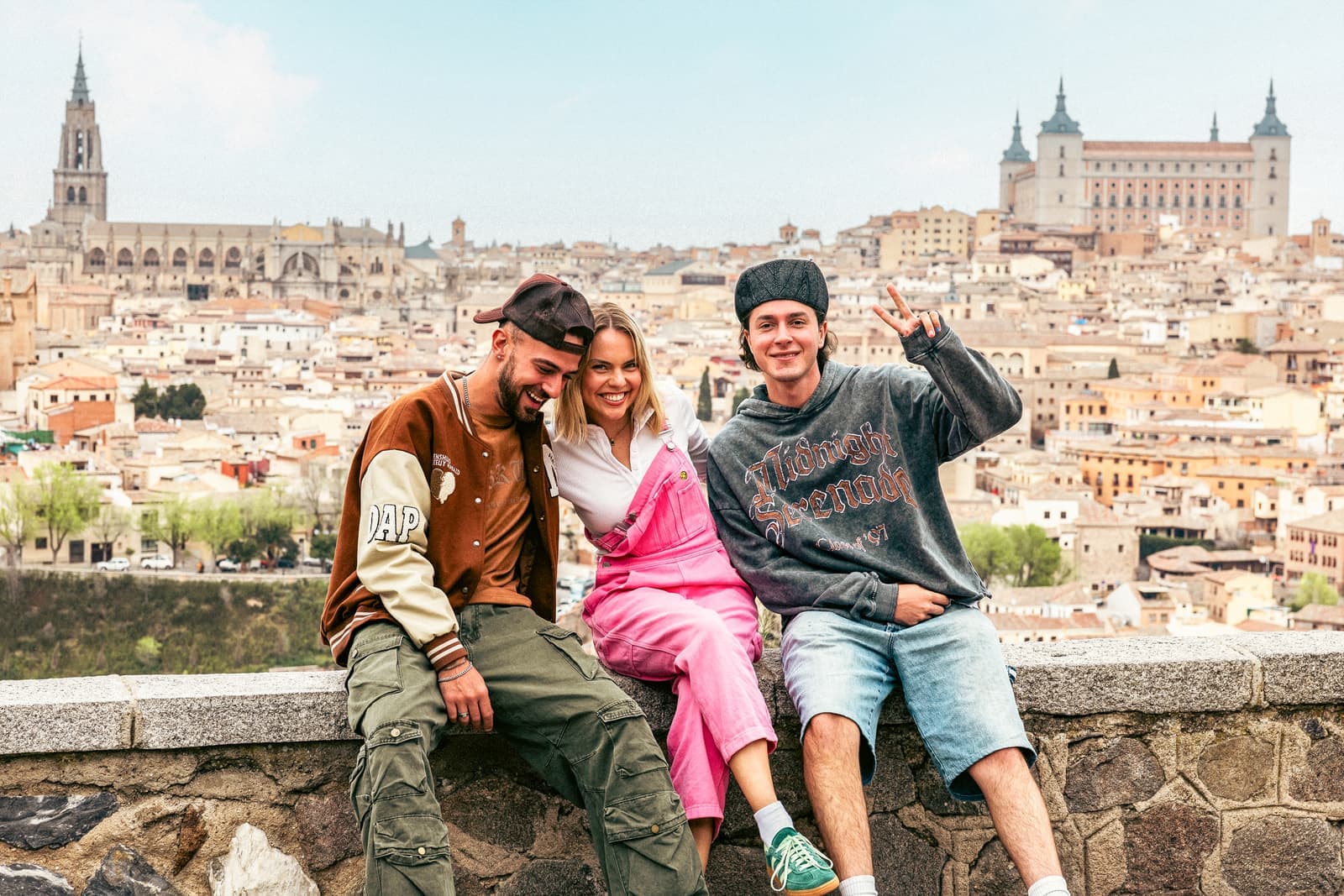 Three travellers sat on wall of viewpoint in front of the city of Toledo, Spain