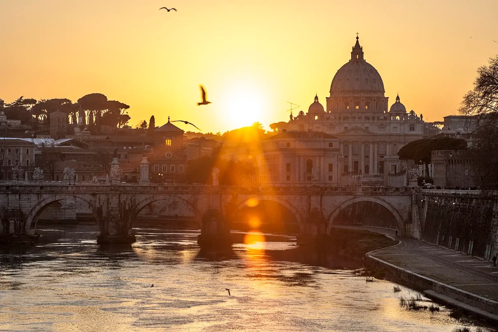 St. Peter’s Basilica and a bridge over the Tiber River in Rome, Italy, at sunset.