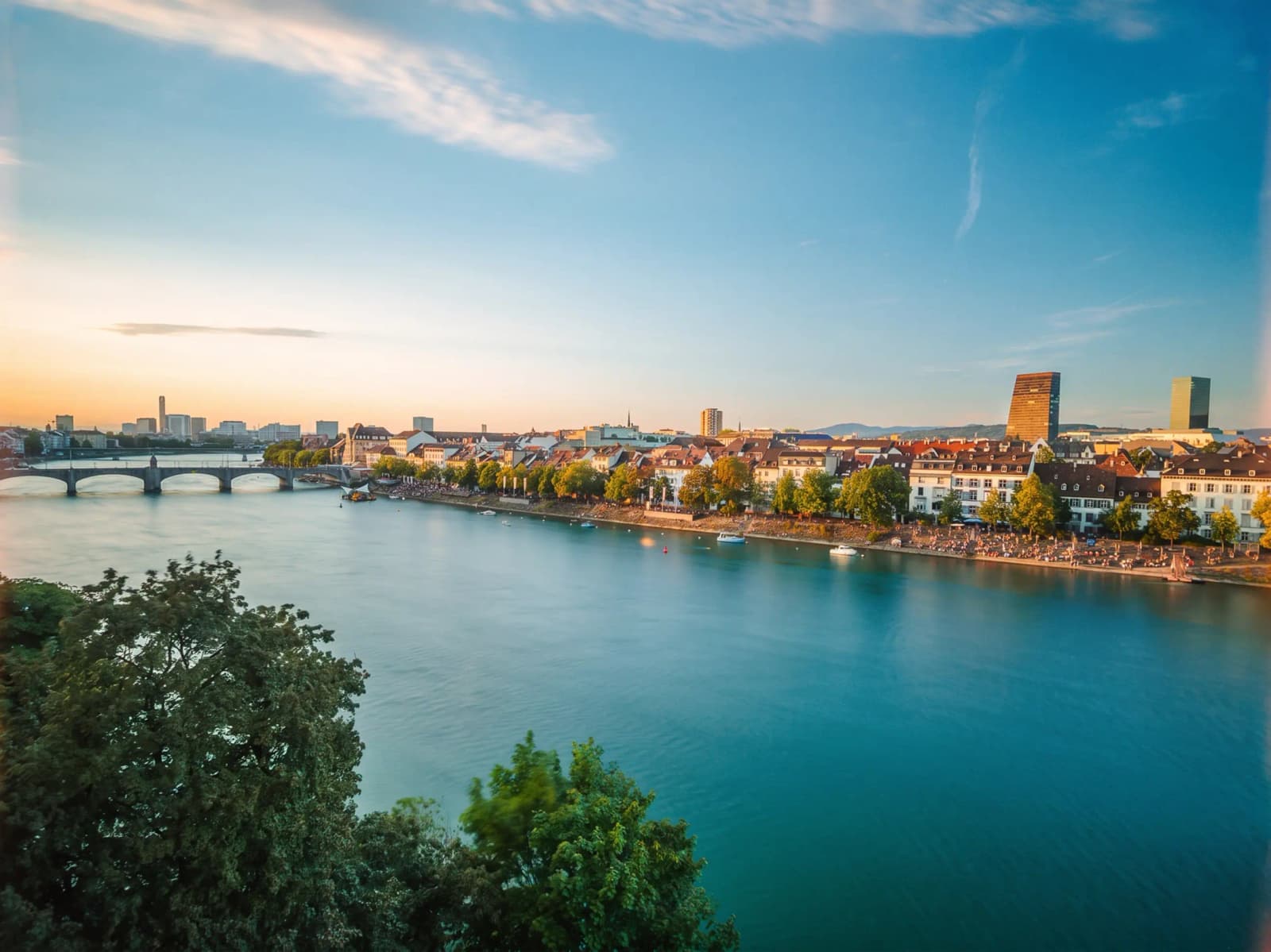 Skyline of Basel, Switzerland, along the Rhine River, with bridges and riverside buildings stretching across the waterfront.