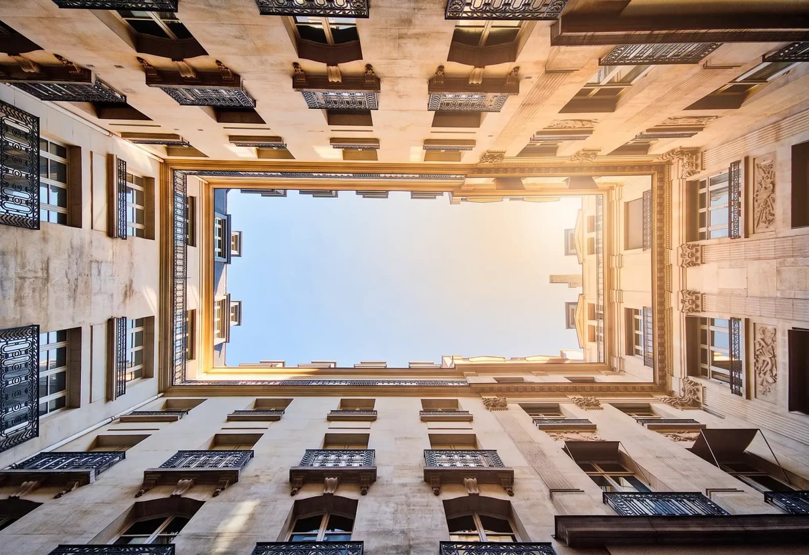 Looking up at the inner courtyard of a building, with balconies and windows surrounding an open view of the sky.