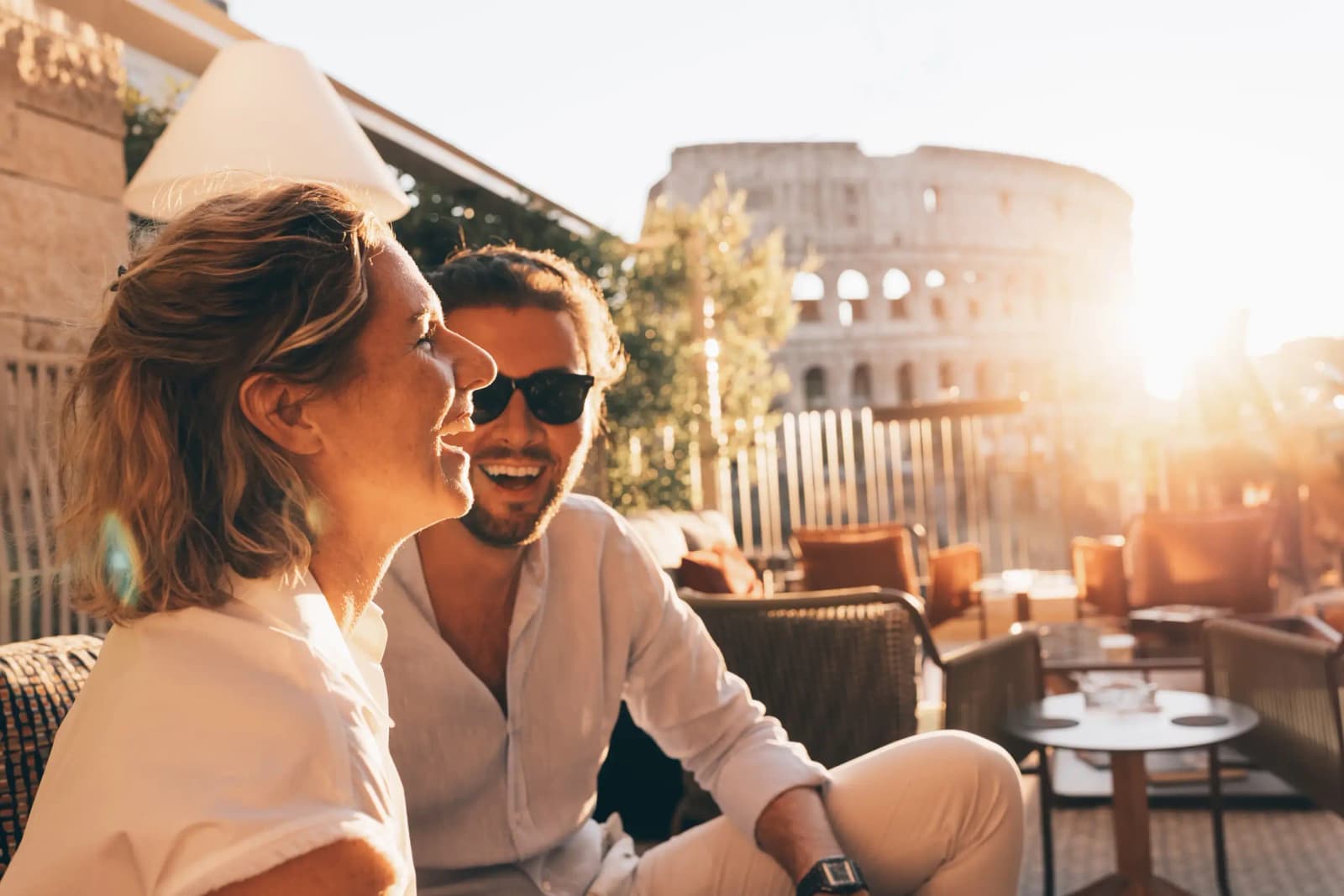 People seated on a rooftop terrace with the Colosseum in Rome, Italy, in the background.