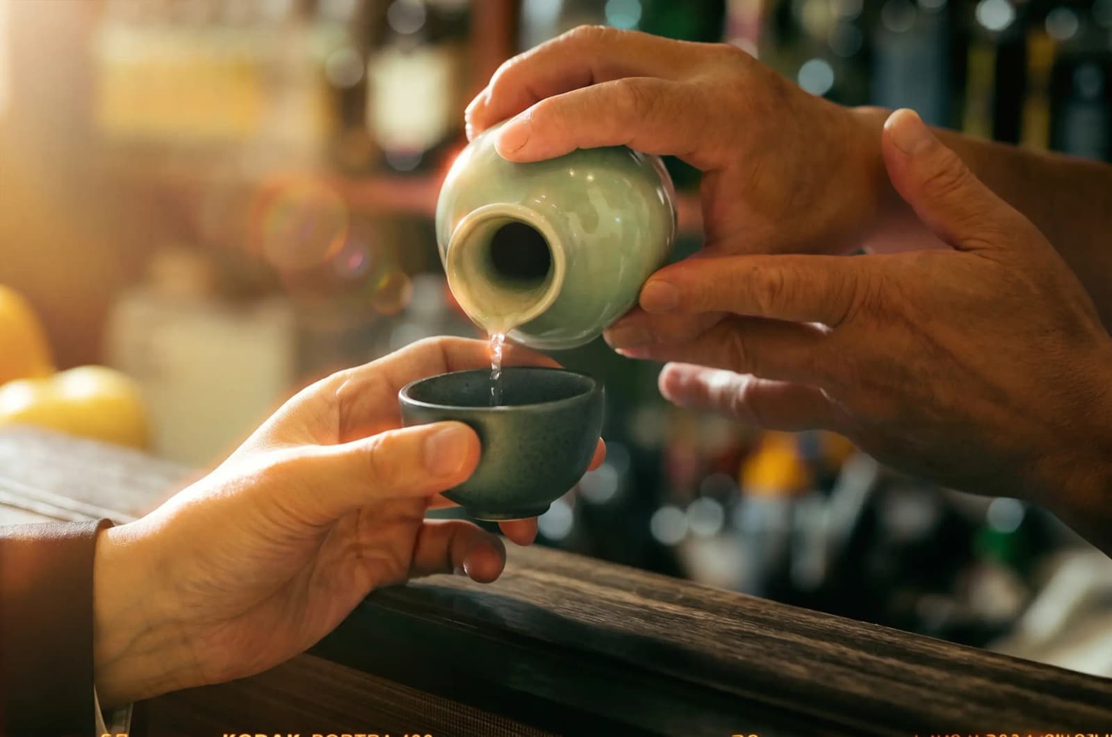 Sake being poured from a ceramic bottle into a small cup.