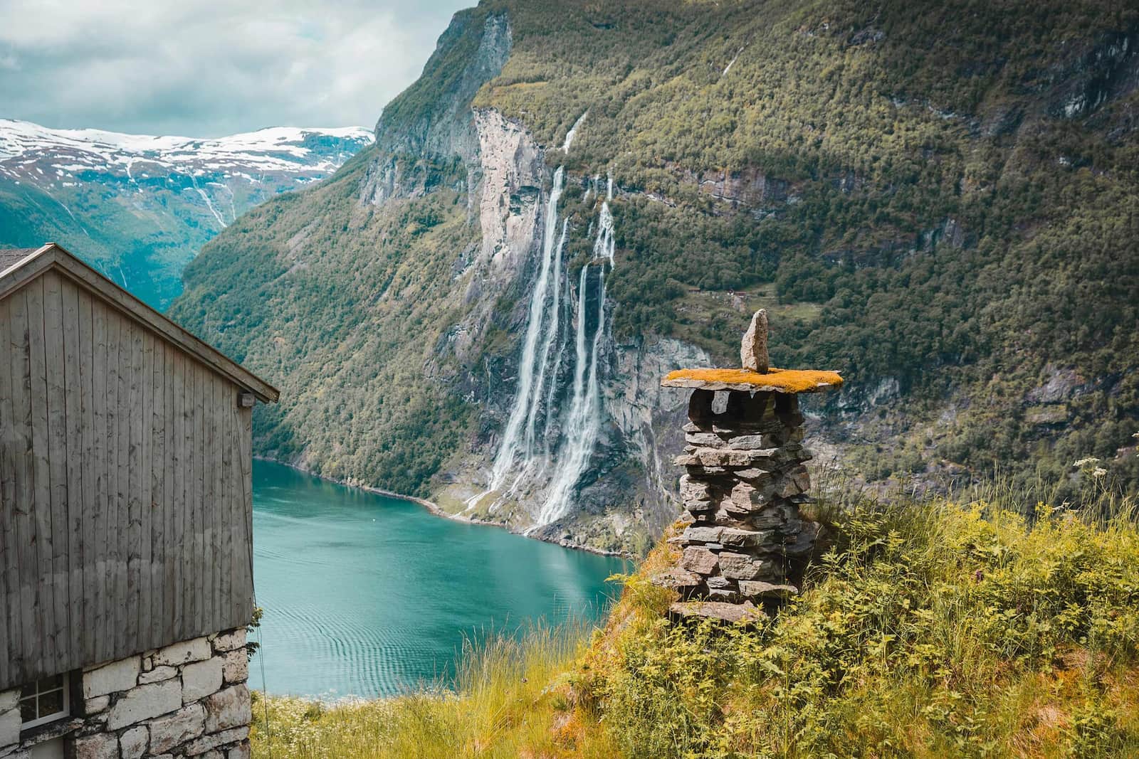 Seven Sisters waterfall cascading into turquoise Geirangerfjord with wooden cabin in foreground