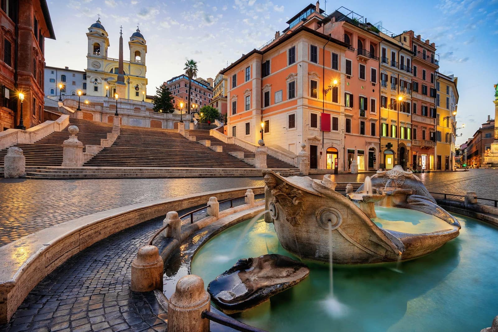 Barcaccia Fountain at Spanish Steps in Rome with illuminated buildings and Trinità dei Monti church
