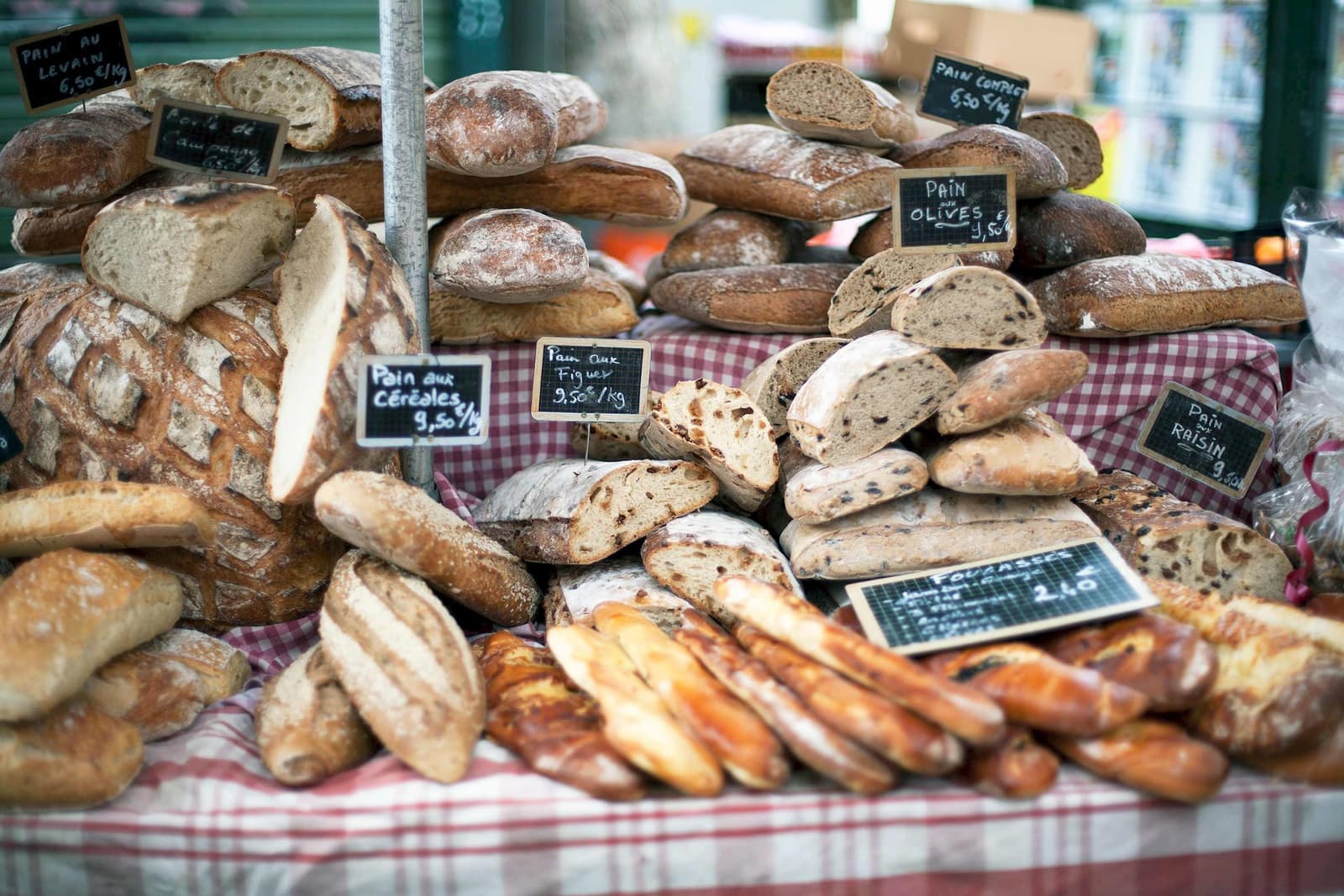 Rustic bakery table with assorted breads and handwritten sign on checkered cloth