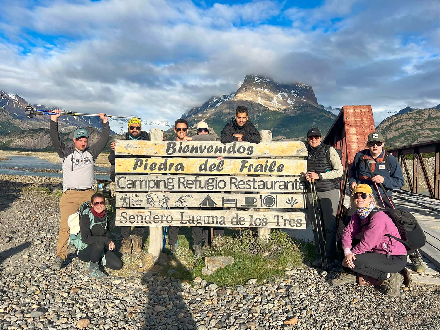 Nine travellers standing next to the Laguna de los Tres sign with mountains in the background in El Chalten, Patagonia