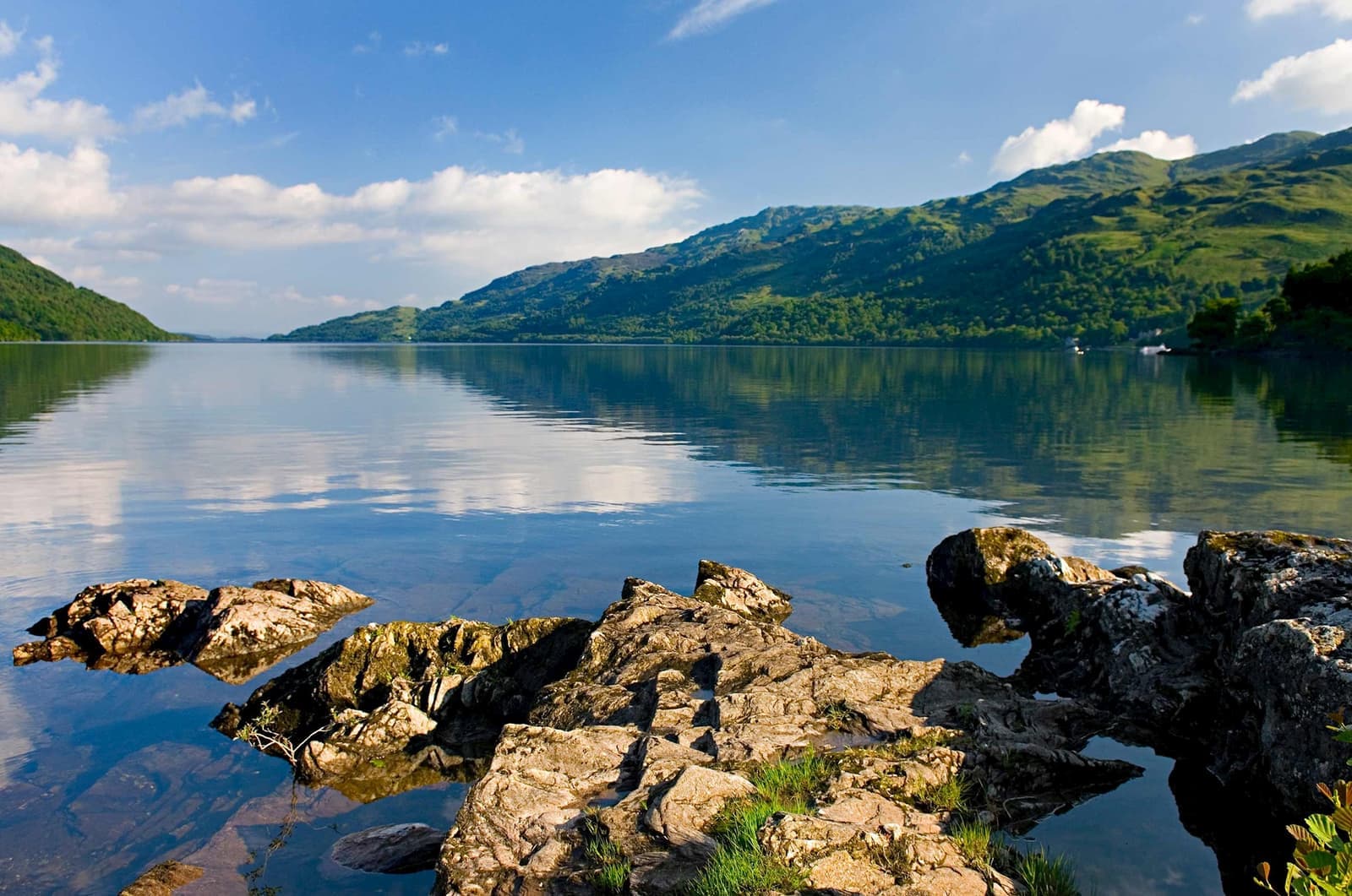 Rocky shoreline overlooking calm waters of Loch Lomond with green hills in background