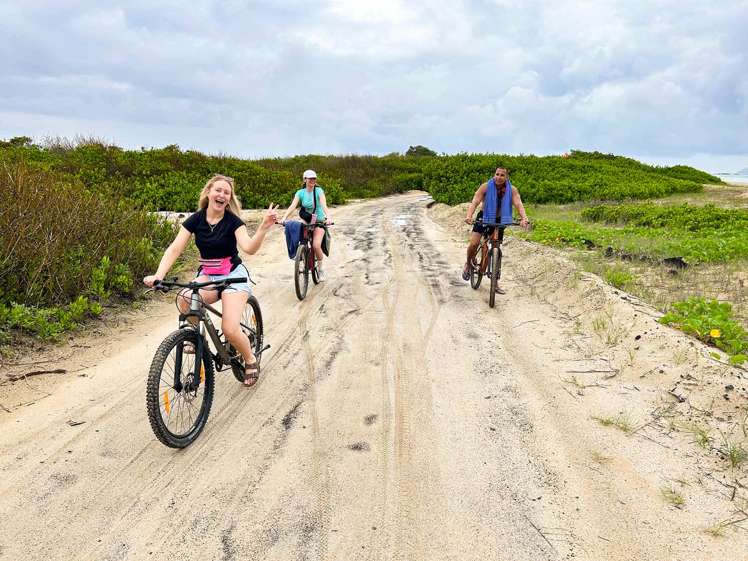 Three travellers riding bikes along the sand on San Cristobal Island, Ecuador