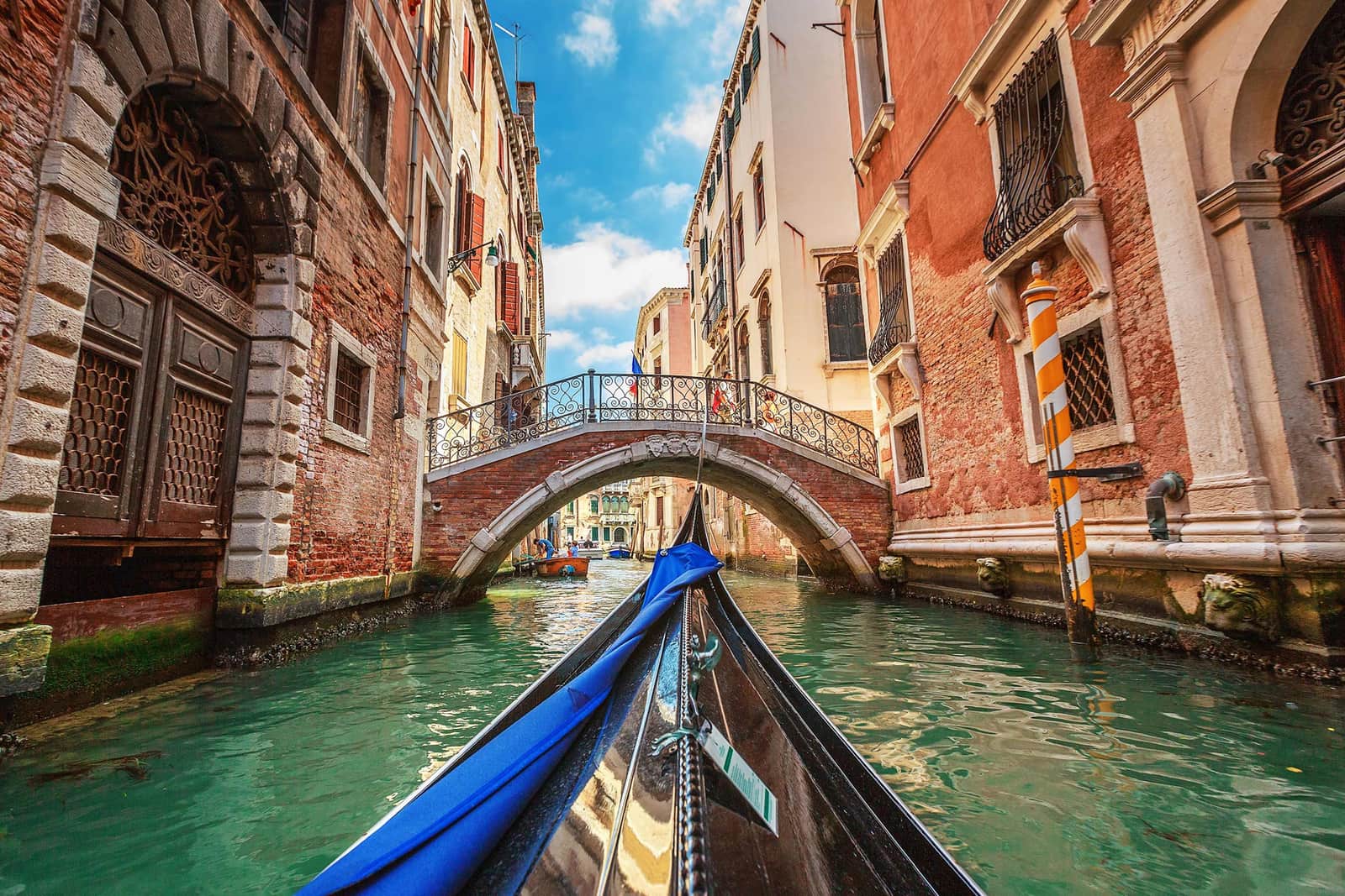 Gondola approaching iron bridge on Venetian canal with historic building