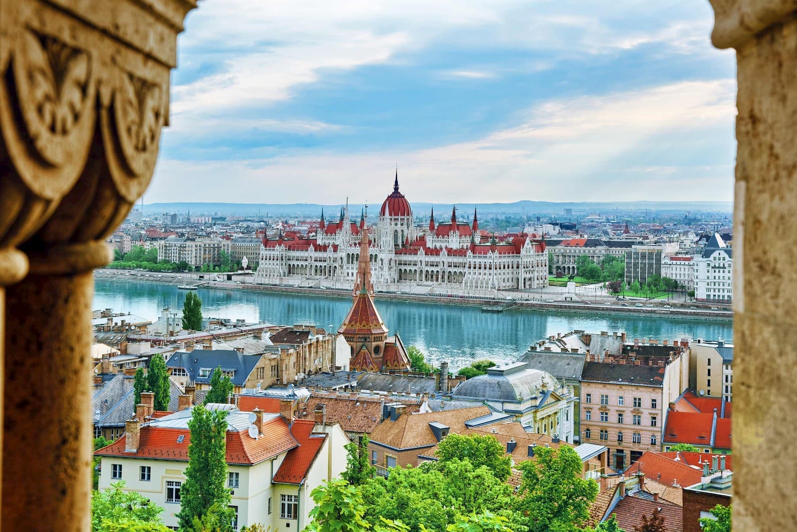 Panoramic view of Hungarian Parliament beside Danube River with rooftops and trees