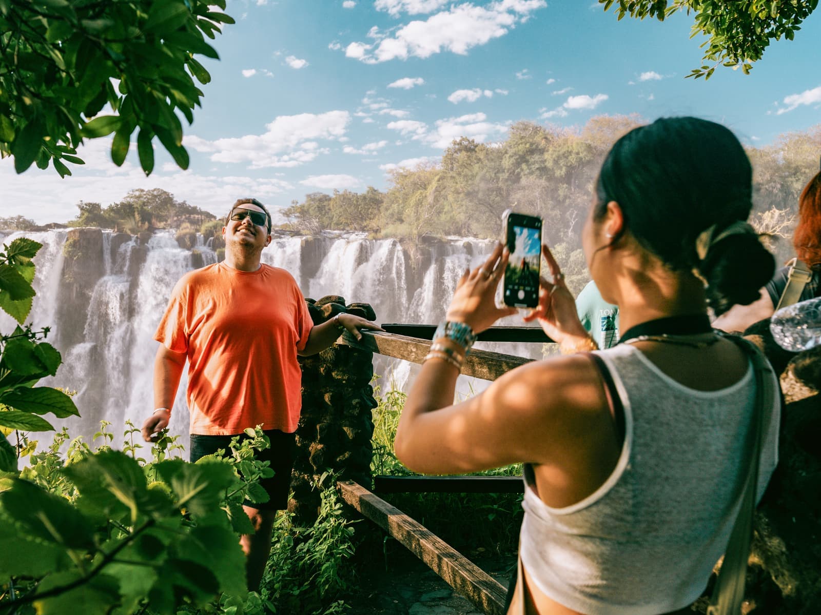 Traveller taking a photo of friend stood at view point overlooking Victoria Falls, Zambia