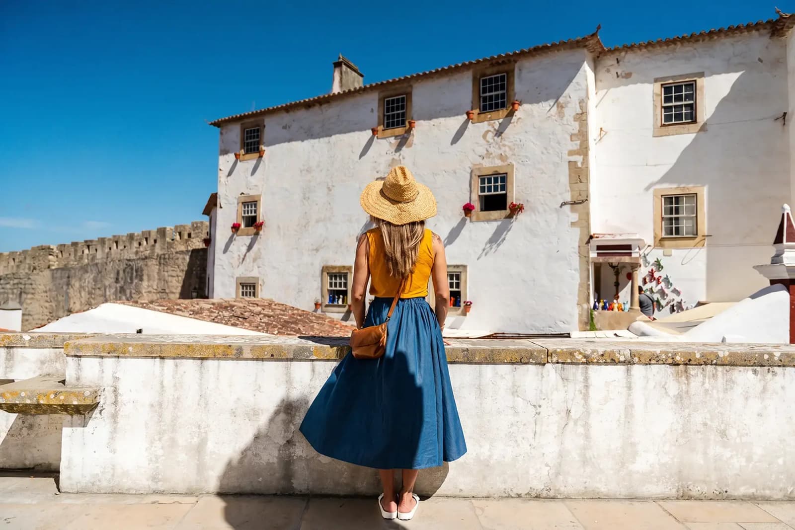 Person standing beside whitewashed buildings and stone walls in Óbidos, Portugal.