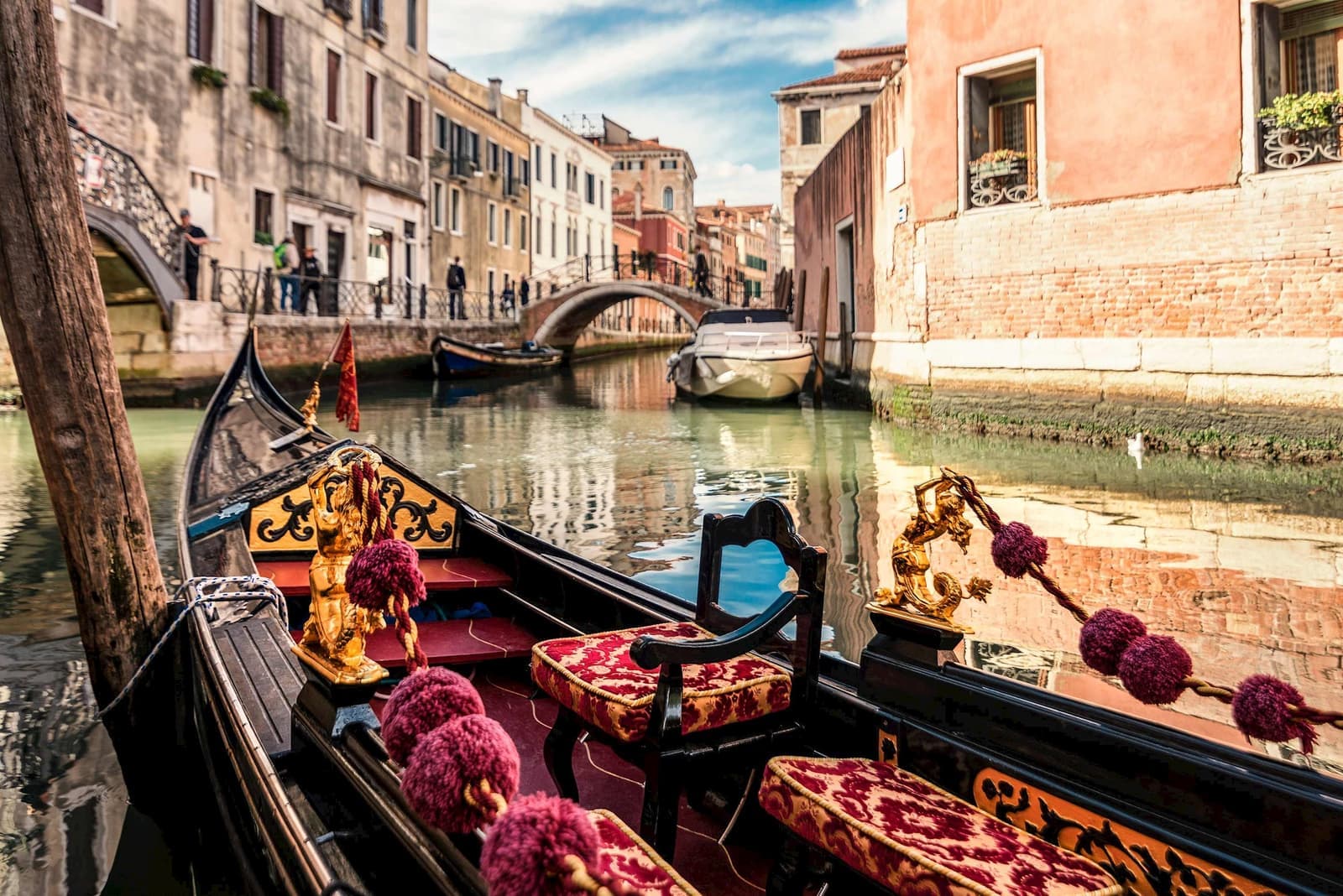 Gondola with velvet seats and golden decorations on Venetian canal near stone bridge
