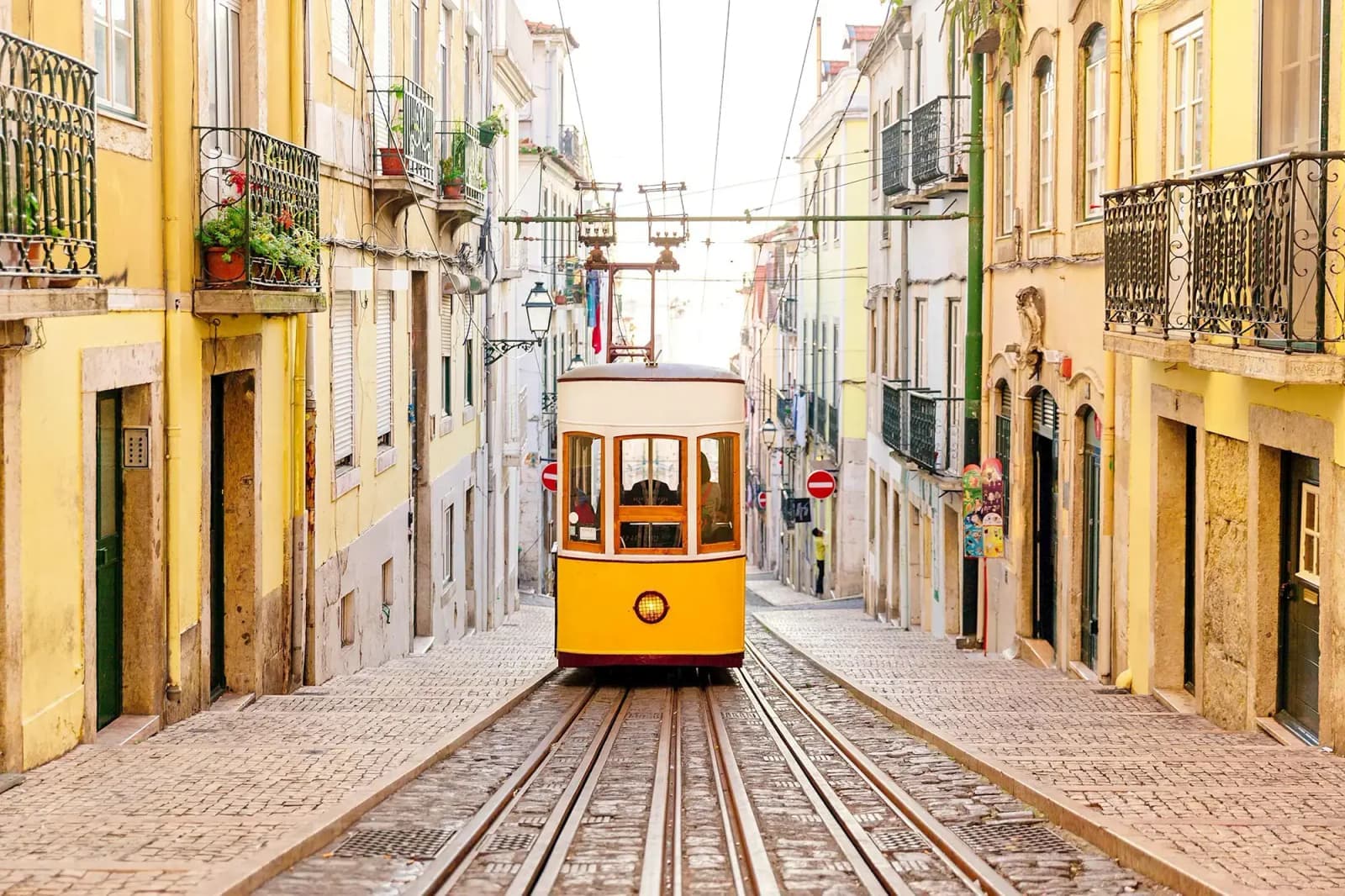 Yellow tram on steep cobblestone street in Lisbon’s historic district