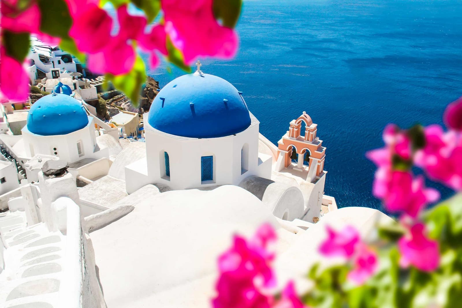 Blue-domed church framed by pink flowers in Santorini, Greece