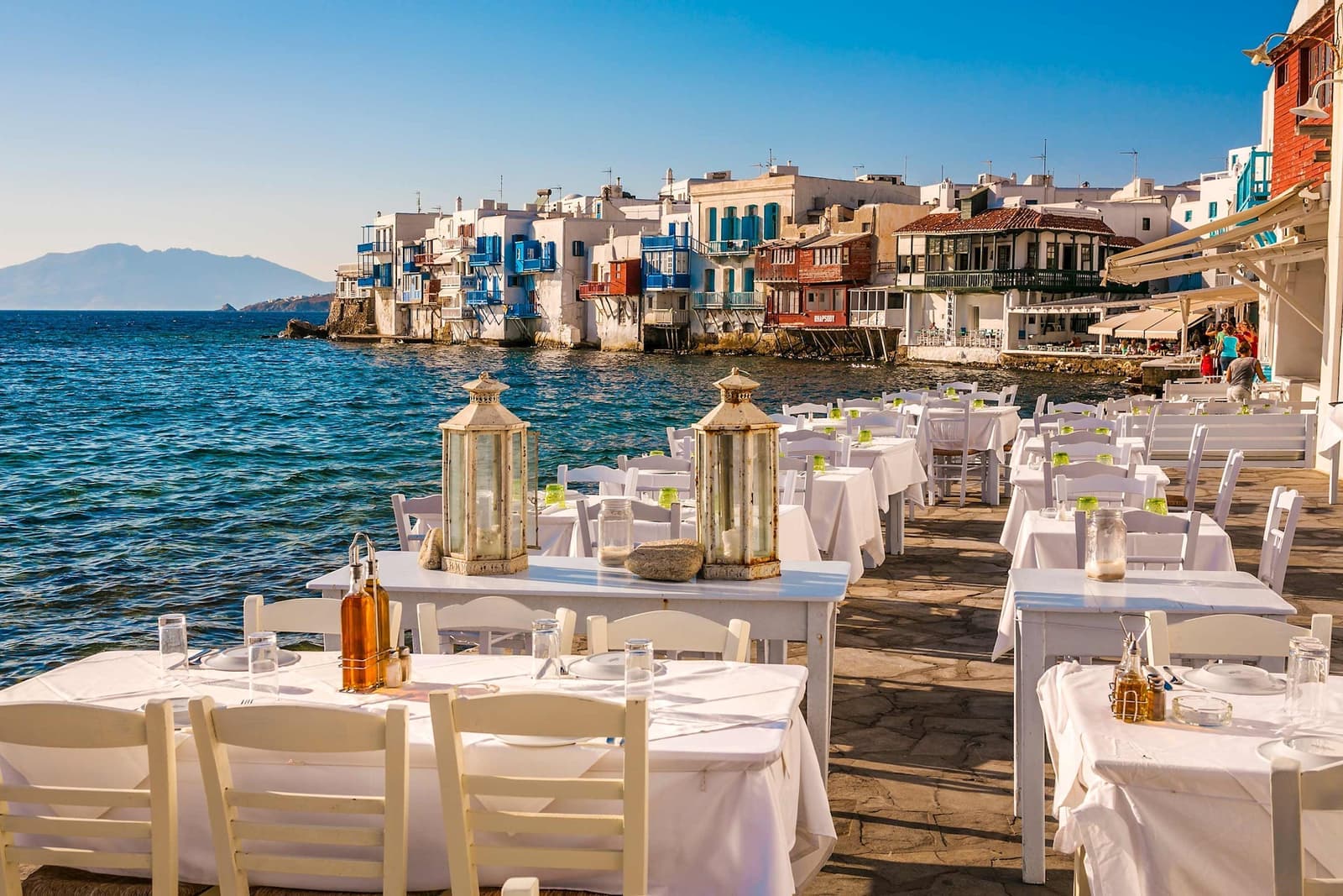 Seaside restaurant tables overlooking calm blue waterin Little Venice, Mykonos, Greece