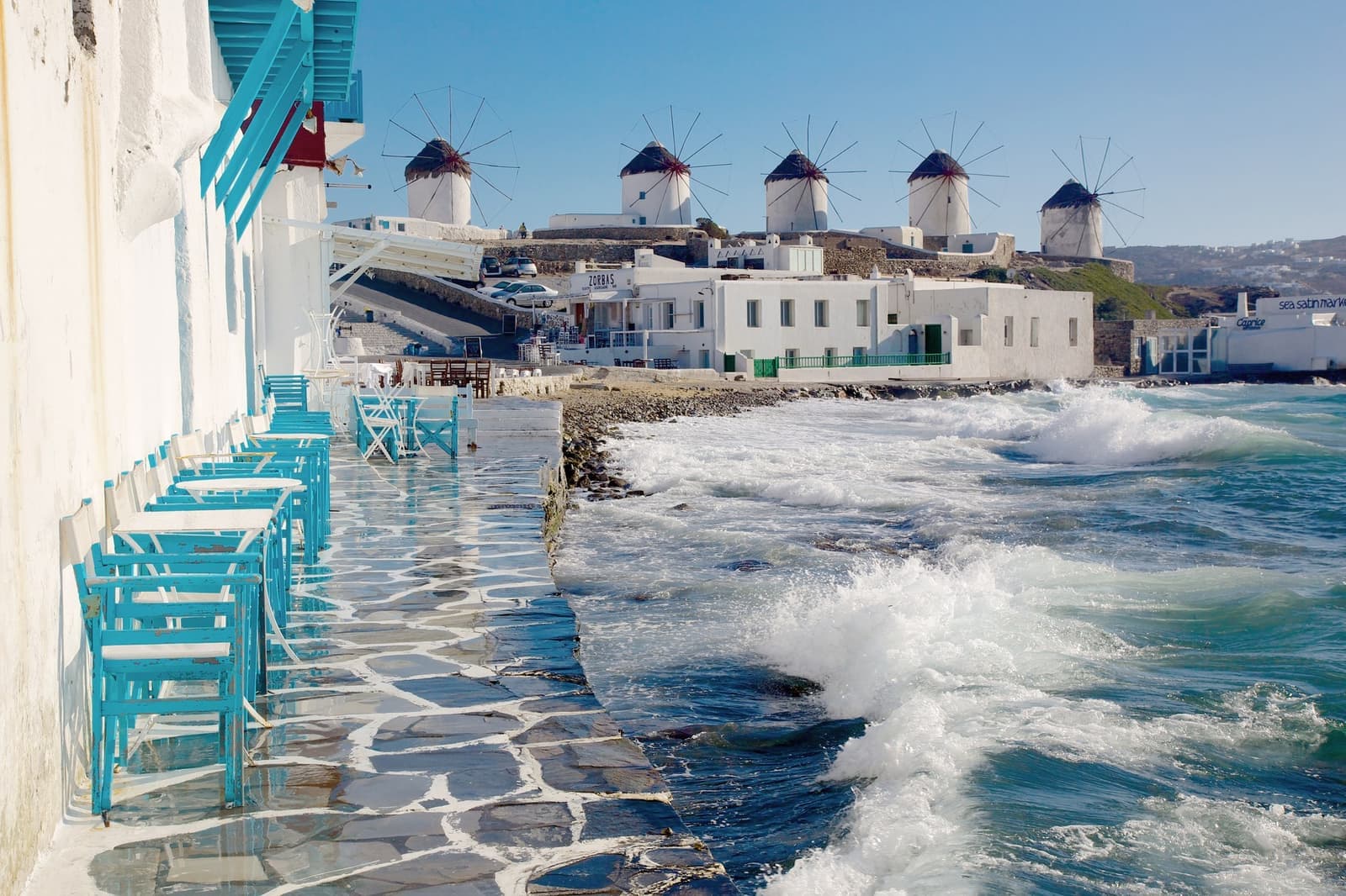 Seaside bar on the water with a view of windmills in Mykonos, Greece.