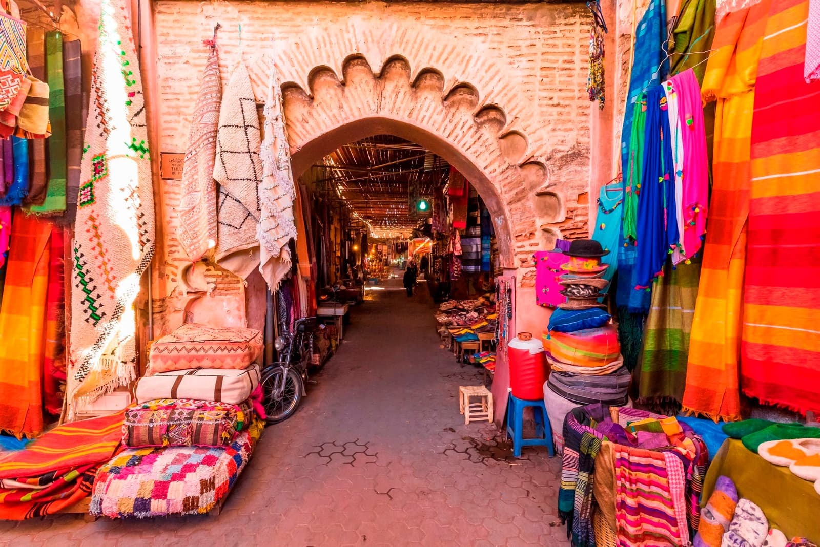 Colourful textiles and rugs displayed at an arched entrance to a Moroccan souk