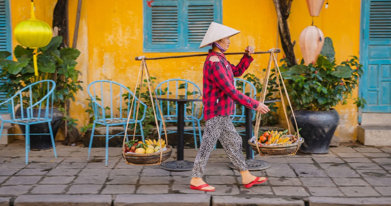Person walking past bright yellow wall with potted plants, Hoi An, Vietnam
