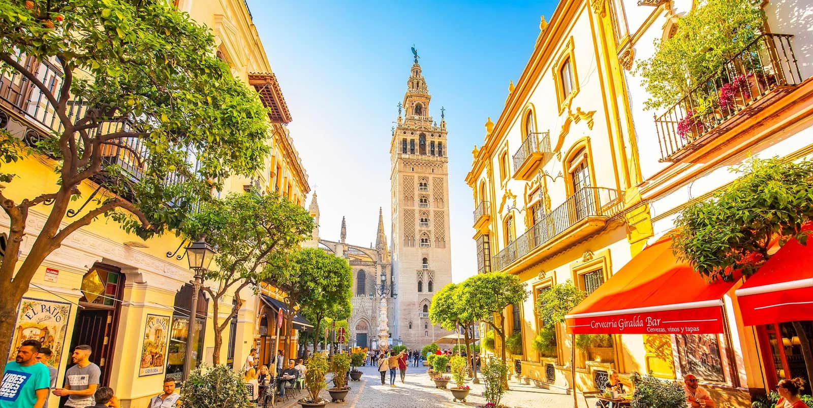 Historic street lined with colourful buildings and tall cathedral tower in Seville, Spain