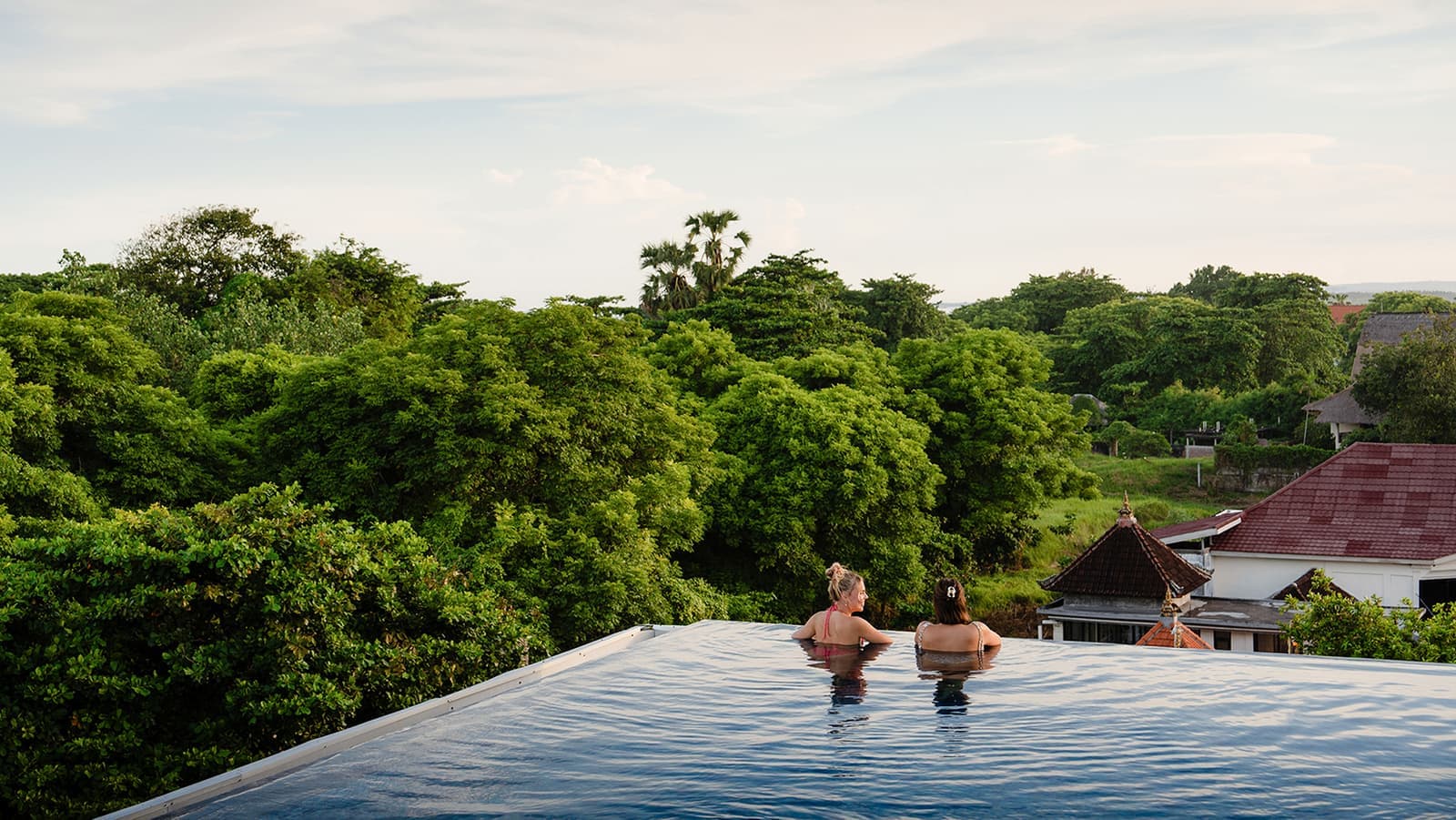 Two travellers looking at trees whilst in an infinity pool in Sanur, Indonesia