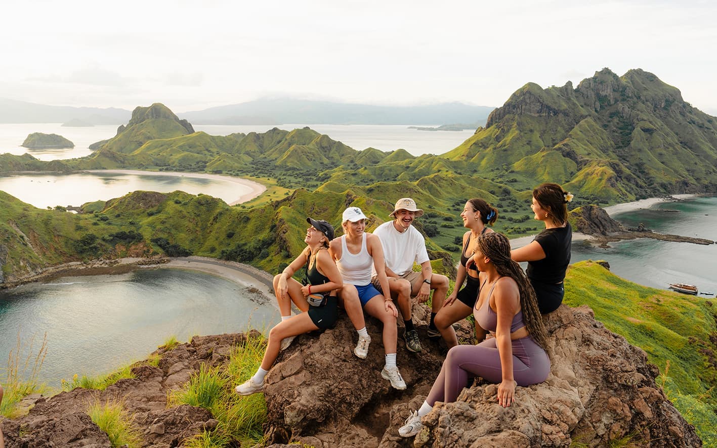A group of travellers sitting at the top of a mountain overlooking the view of Padar Island, Indonesia