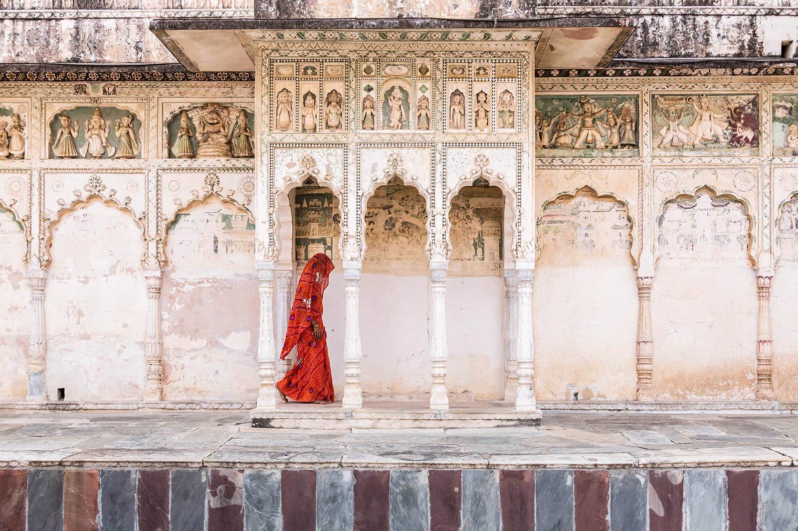 Woman in red walking past ornate, ancient Indian temple walls, Pushkar, India
