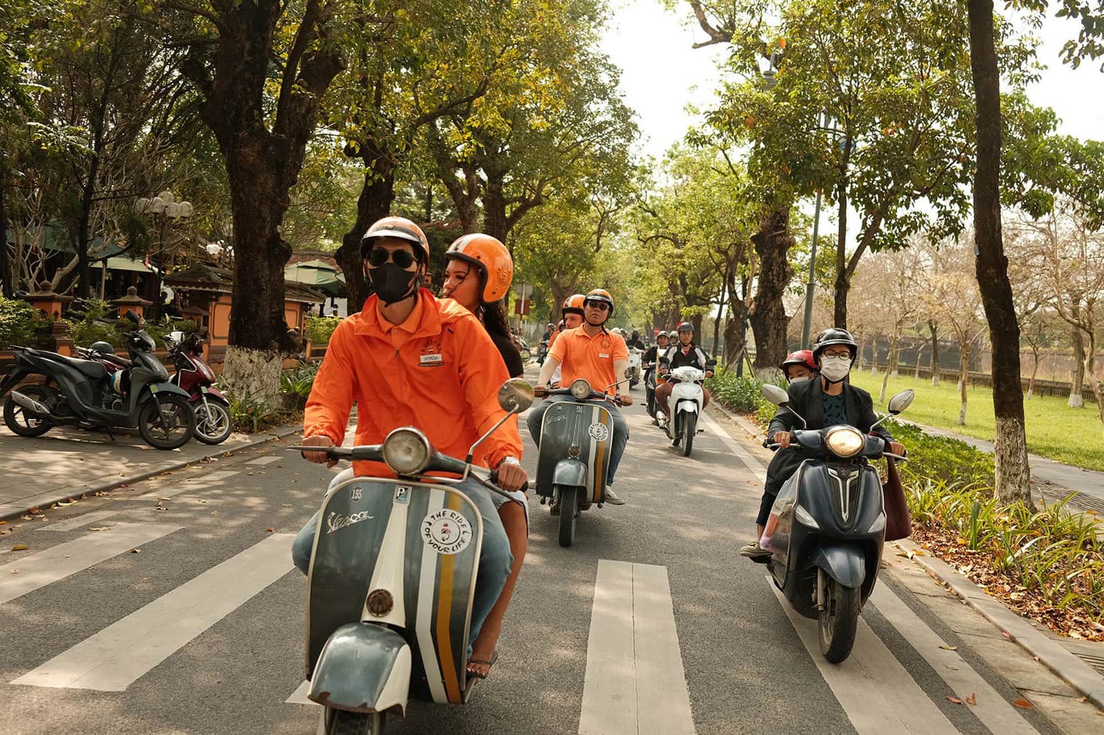 Travellers on back of motorbikes riding down tree-lined street, Hue, Vietnam