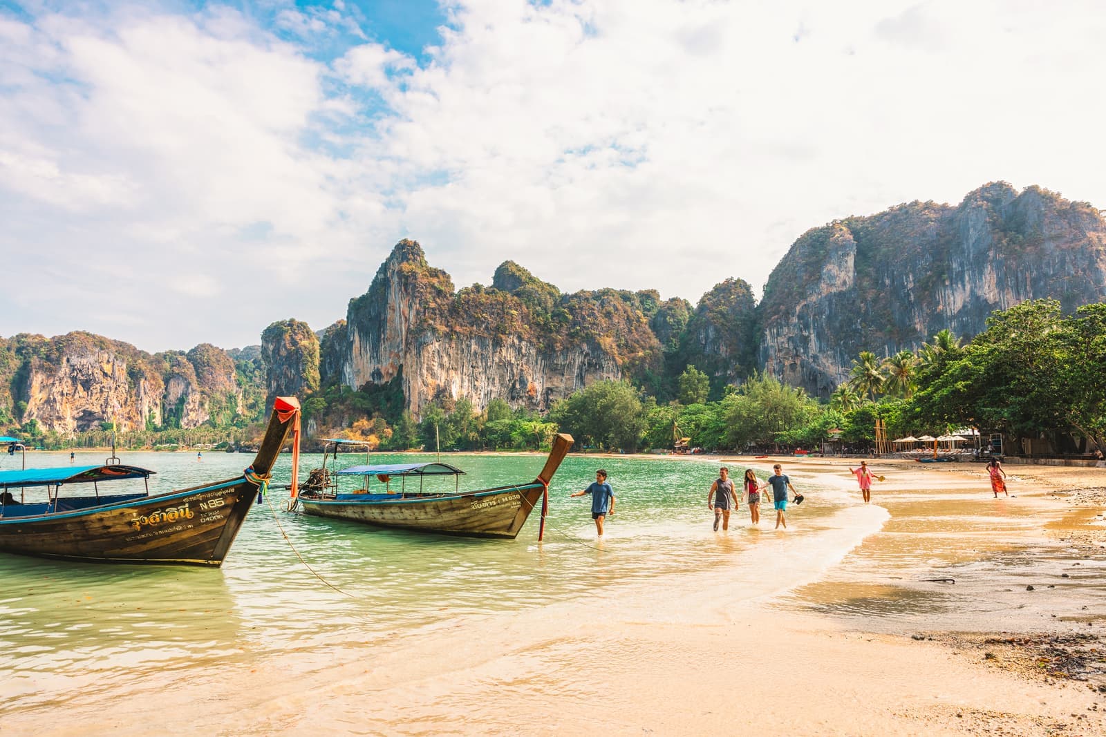 Travellers walking along beach towards boats, Krabi, Thailand
