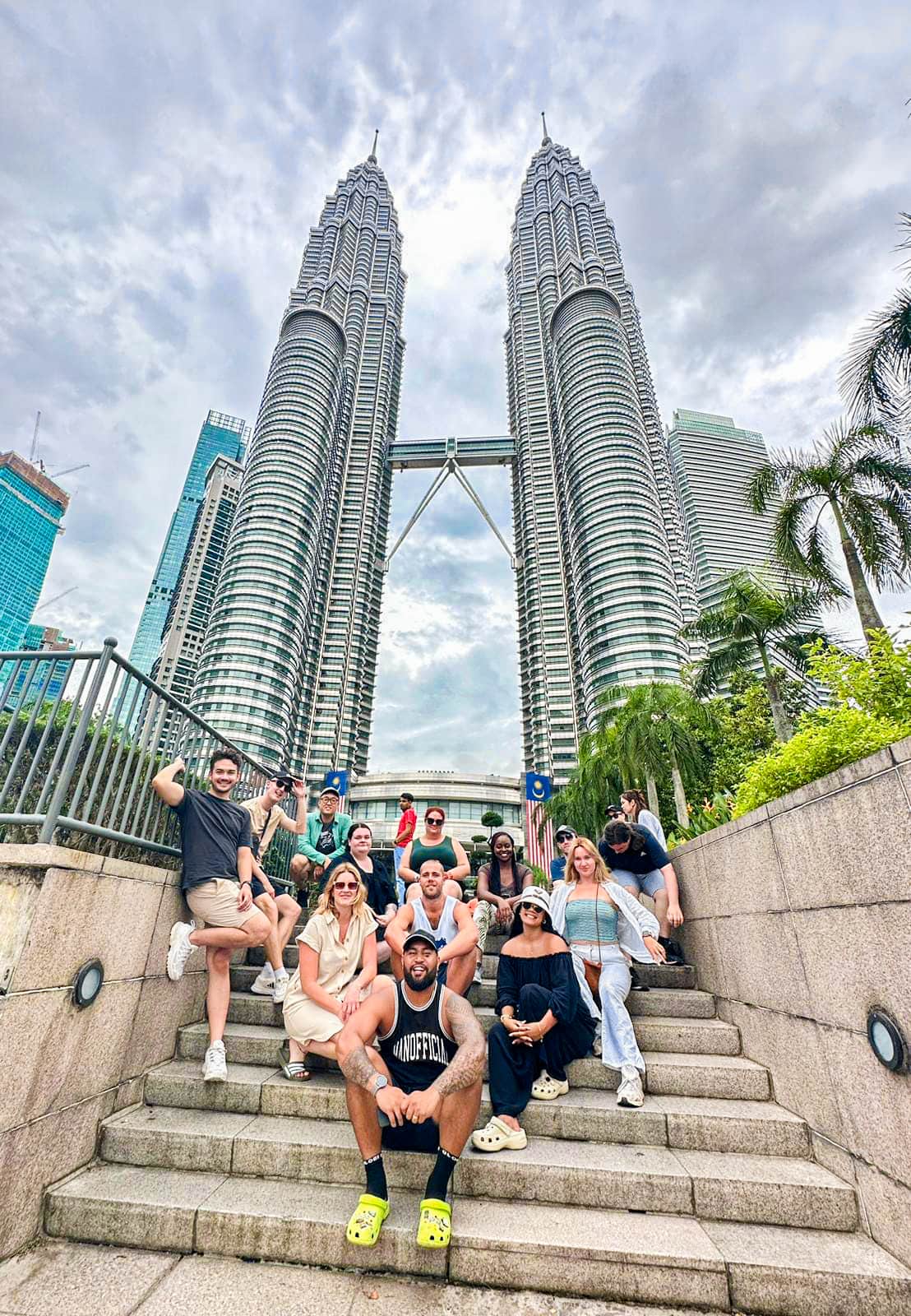 Group of travellers sitting on steps with the Petronas Twin Towers soaring in the background
