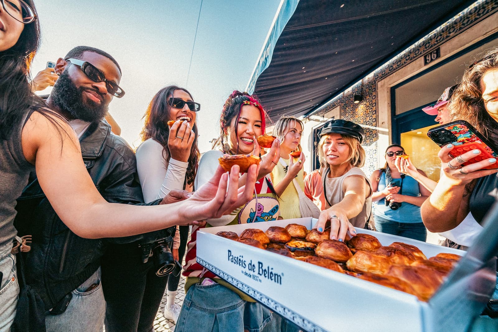 Travellers helping themselves to box of pastries from Pastéis de Belém, Lisbon, Portugal