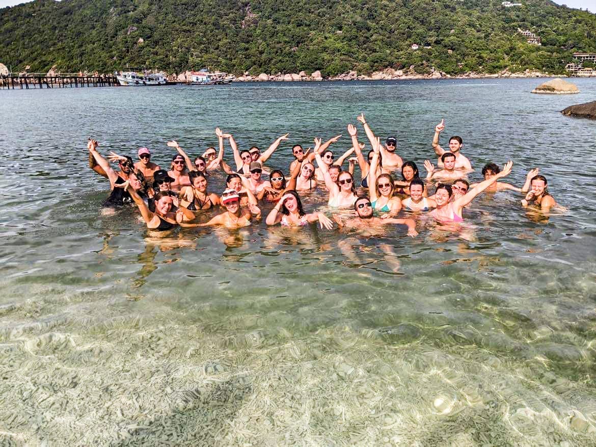 Group of travellers with their arms up in the air in the shallow waters of Koh Tao, Thailand
