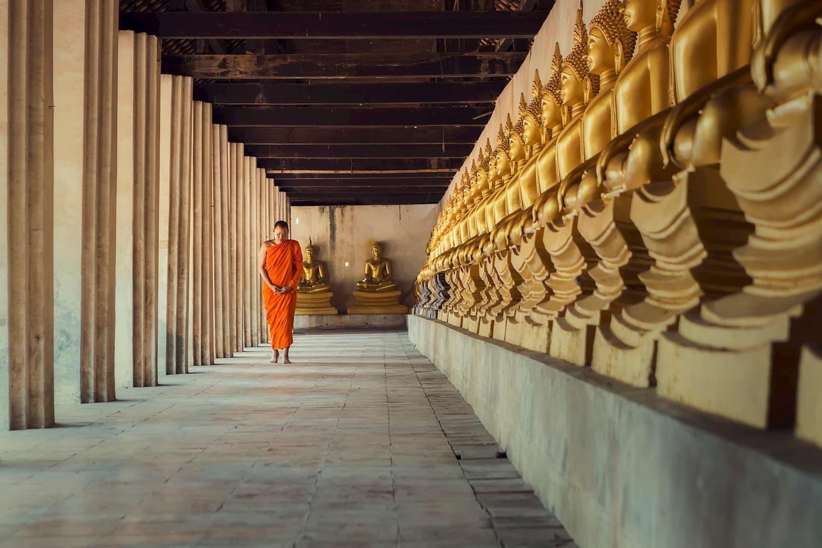 Monk walking along corridor lined with golden Buddha statues, Ayutthaya, Thailand