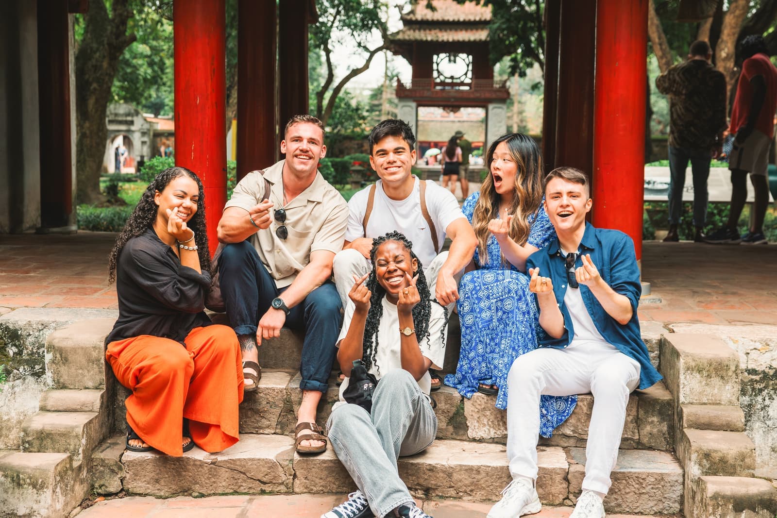 Travellers sat on the steps of the Temple of Literature making a heart hand gesture, Hanoi, Vietnam