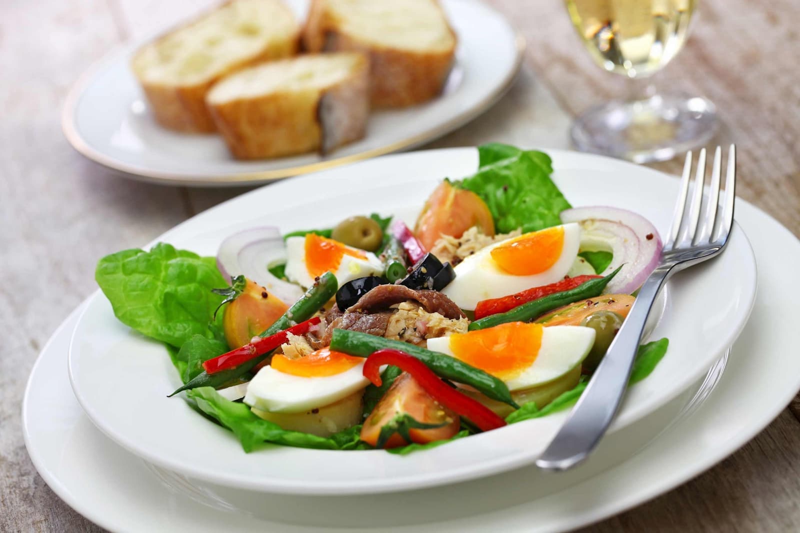 Niçoise salad on a plate with eggs, tuna, vegetables and bread